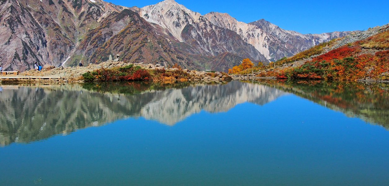 Stunning view of Hakuba’s autumn foliage at Tsugaike, with vibrant fall colors and mountain reflection on a clear blue lake in the Japanese Alps