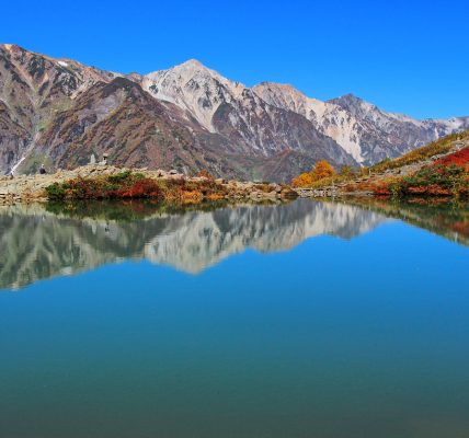 Stunning view of Hakuba’s autumn foliage at Tsugaike, with vibrant fall colors and mountain reflection on a clear blue lake in the Japanese Alps
