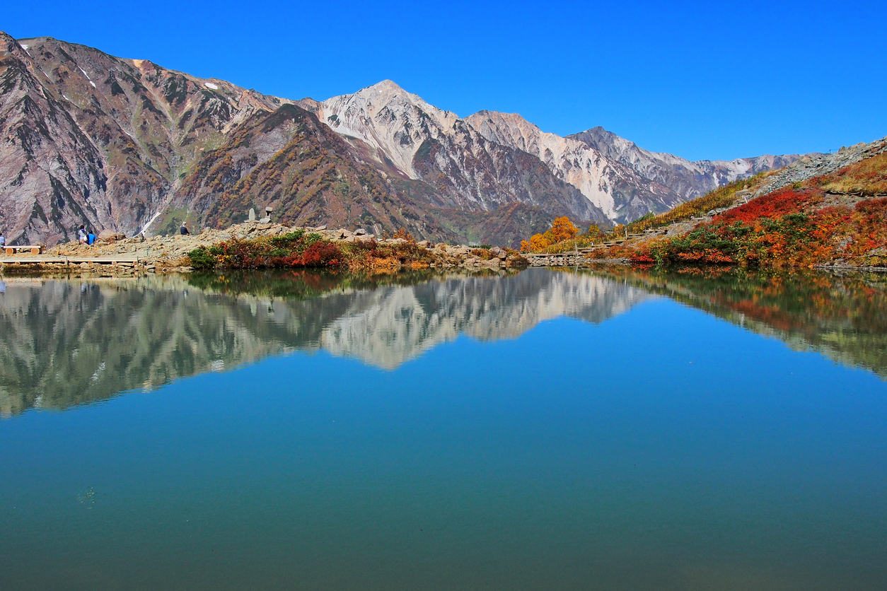 Stunning view of Hakuba’s autumn foliage at Tsugaike, with vibrant fall colors and mountain reflection on a clear blue lake in the Japanese Alps